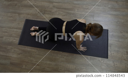 Beautiful sporty girl practicing yoga or pilates at home. Media. Top view of a woman doing balance exercise and stretching her arm and leg. Beautiful sporty girl practicing yoga or pilates at home. Media. Top view of a woman doing balance exercise and stretching her arm and leg. 114848543
