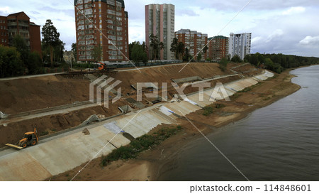 Aerial view of construction site on city embankment next to the river. Clip. Process of improving pedestrian road. 114848601