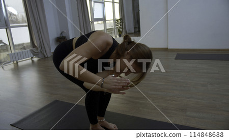 Young woman is doing yoga in a white room filled with light. Media. The girl performs yoga stands and elements near the large window. Young woman is doing yoga in a white room filled with light. Media. The girl performs yoga stands and elements near the large window. 114848688