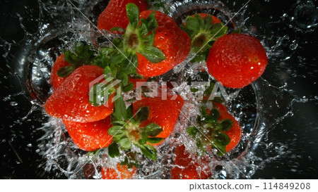 Fresh pieces of strawberries falling into water, top down view, black background 114849208