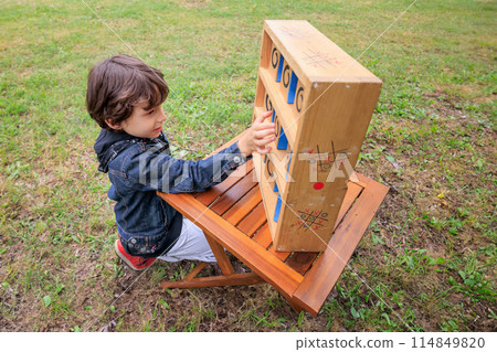 Child playing wooden Tic-Tac-Toe game outdoors in park 114849820