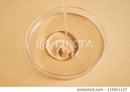 Serum or cosmetic oil flows into a transparent bowl. 114851127