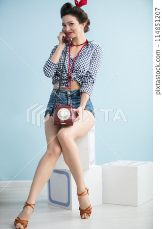 Woman in the style of the fifties. Beautiful retro woman with a phone on a blue background. Woman in the style of the fifties. Beautiful retro woman with a phone on a blue background. 114851207