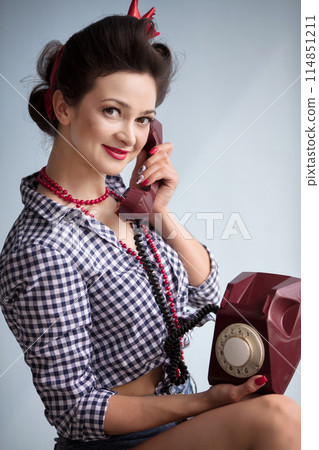 Woman in the style of the fifties. Beautiful retro girl talking on an old telephone. Woman in the style of the fifties. Beautiful retro girl talking on an old telephone. 114851211
