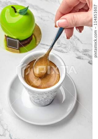 Female hand stirring espresso served with green apple-shaped pastry Female hand stirring espresso served with green apple-shaped pastry 114851607
