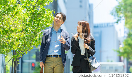 微笑的商人和婦女走在街上有樹的辦公區 微笑的商人和婦女走在街上有樹的辦公區 114851892