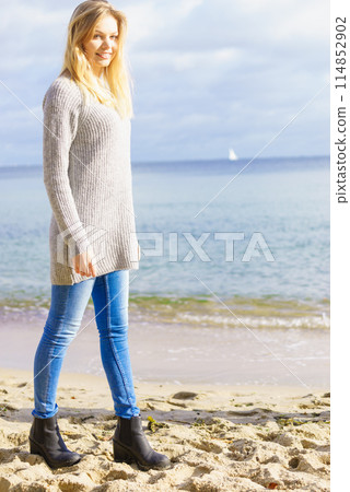 Woman in sweater walking on beach 114852902