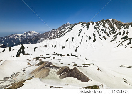 Aerial view of a mountain hut standing in the remaining snow in May, and Mount Tsurugi from Tsurugi-Gozen, with a view of Mount Tsurugi and the three mountains of Kekatsu. 114853874