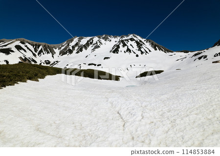 Aerial view of the remaining snow on Mt. Tateyama's Murodo Plain in May, as it begins to melt. Midorigaike Pond and the towering Tateyama mountain range. 114853884