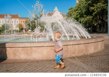 Child run and play on street fountain on Szombathely in Hungary. Boy have fun near fountain at Szombathely main square. Traveling in Szombathely city, Hungary. Child run and play on street fountain on Szombathely in Hungary. Boy have fun near fountain at Szombathely main square. Traveling in Szombathely city, Hungary. 114854136