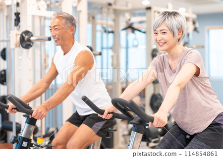 Senior men and women training on exercise bikes Senior men and women training on exercise bikes 114854861