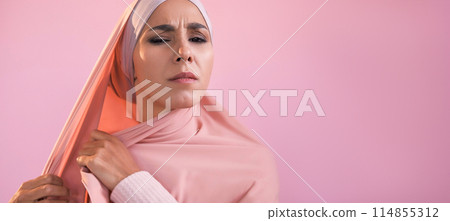 Annoying hijab. Social pressure. Female rights. Gender equality. Frustrated angry upset woman covering head wearing muslim headscarf isolated on pink empty space background. Annoying hijab. Social pressure. Female rights. Gender equality. Frustrated angry upset woman covering head wearing muslim headscarf isolated on pink empty space background. 114855312