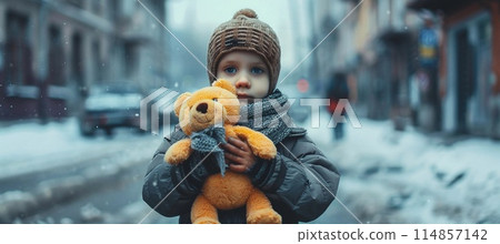 homeless boy with a toy bear in his hands on a snowy city street 114857142