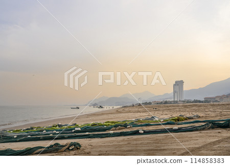 Fishing nets on the sandy sea shore with hotels and mountains on Arabian Peninsula in UAE at sunset 114858383