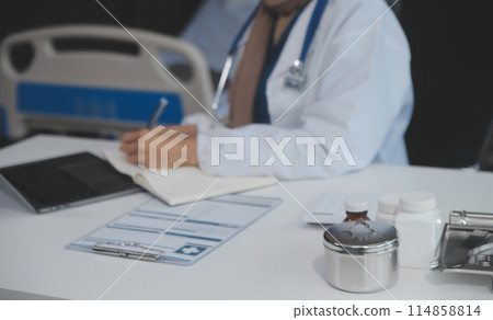 Female doctor sitting at desk and writing a prescription for her patient 114858814