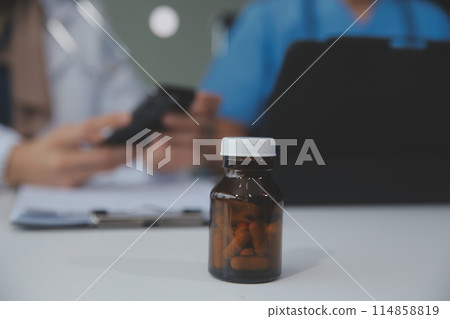 Asian psychologist women pointing on pills bottle to explaining medicine and prescription to female patient while giving counseling about medical and mental health therapy to female patient in clinic. 114858819