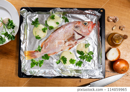 There is carcass of raw fish sea bass with spices on foil. 114859965