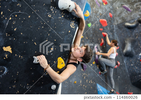 Confident young man scaling artificial climbing wall in climbing gym 114860026