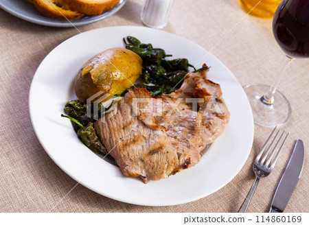 Fried pork tenderloin, garnished with potatoes baked in peel and pieces of bell pepper 114860169