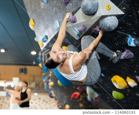 Determined young woman doing her best at climbing artificial wall 114860191