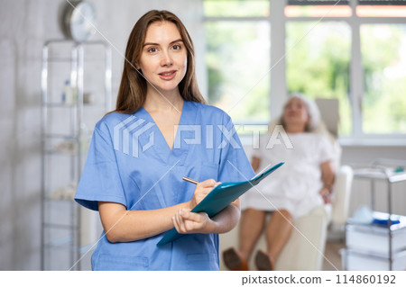 Female doctor in scrub holding clipboard. Female doctor in scrub holding clipboard. 114860192