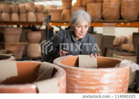 Aged woman selecting decorative earthenware pot in shop 114860285