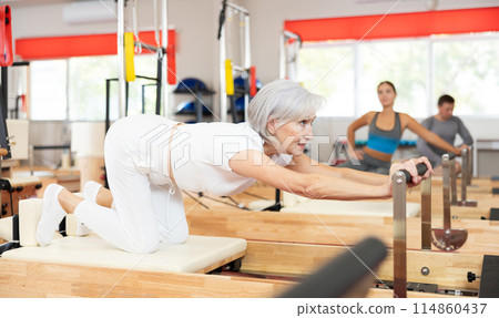 Senior woman performs exercise on reformer to improve coordination, balance, and posture 114860437