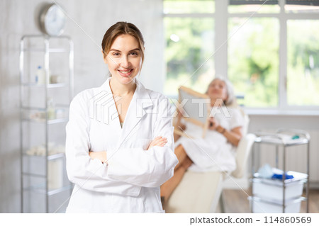 Female doctor cosmetologist stand with woman looking mirror behind in the doctors office. 114860569
