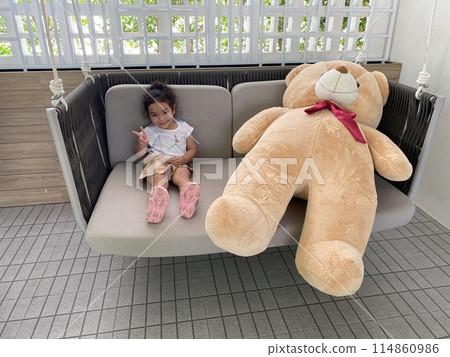 Cute little Asian girl sitting on the couch with teddy bear in the room 114860986