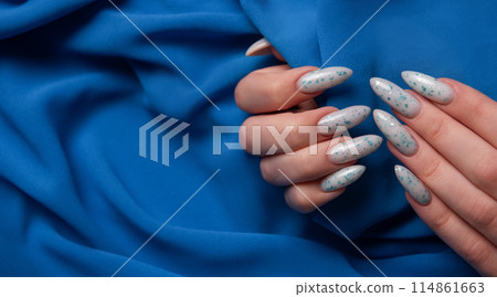 Female hands with blue nail design on blue textile background. Female hands with blue nail design on blue textile background. 114861663