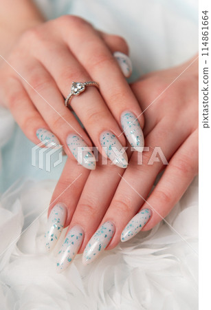 Elegant Hands Featuring Sparkling Ring and Blue Floral Manicure on Delicate White Fabric 114861664