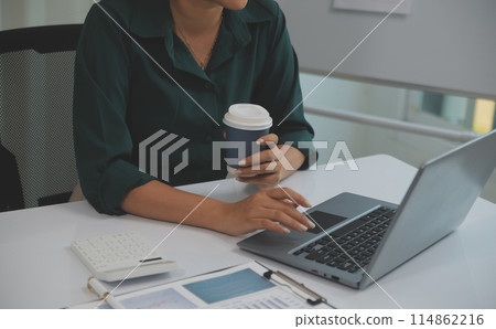 Beautiful young smiling Asian businesswoman working on laptop and drinking coffee, Asia businesswoman working document finance and calculator in her office. Beautiful young smiling Asian businesswoman working on laptop and drinking coffee, Asia businesswoman working document finance and calculator in her office. 114862216