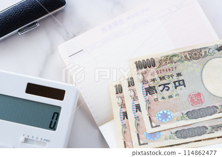 An open bank passbook, 10,000 yen notes, a calculator, and a personal seal are placed on a table 114862477