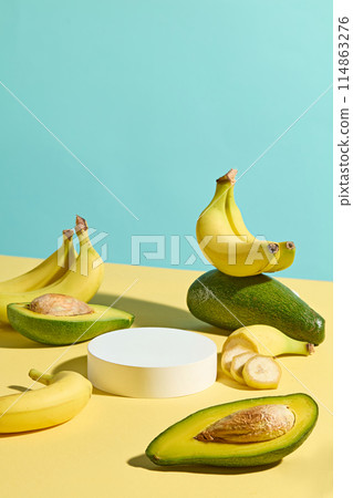 Creative design with high angle view at a yellow table containing fresh fruit like banana and avocado with a circular pedestal of white in center. Displaying or presentation space Creative design with high angle view at a yellow table containing fresh fruit like banana and avocado with a circular pedestal of white in center. Displaying or presentation space 114863276