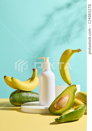 Advertising photo with fresh fruit ingredient for cosmetic product concept, a round platform containing a white blank label bottle of cosmetic above, decorated with fresh avocado and banana around 114863278
