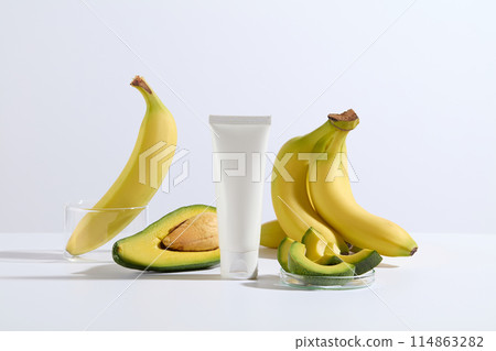 Advertising photo was shot from front view, yellow and green color of banana and avocado striking against white background and a unbranded tube of cosmetic displayed in center, blank space for text 114863282