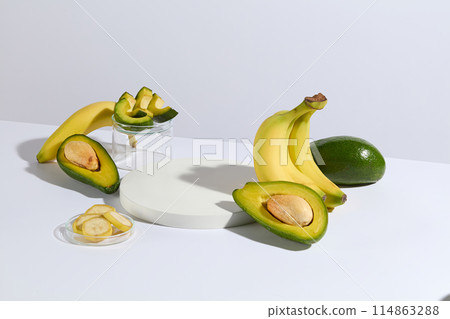 High angle shot at the white flatform containing a few types of fresh fruits for manufacturing natural product consist of avocado and banana with a blank platform for showing product High angle shot at the white flatform containing a few types of fresh fruits for manufacturing natural product consist of avocado and banana with a blank platform for showing product 114863288