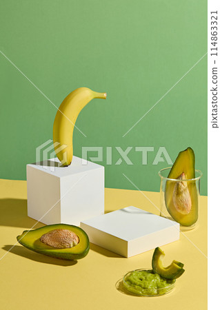 High angle shot photography against green background with yellow countertop contains rectangular white pedestals, yellow ripe banana and fresh avocado decorated around. Displaying and copy space 114863321