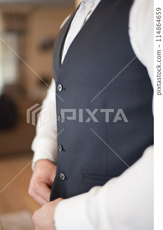 A man in an elegant suit is meticulously adjusting buttons, preparing for a formal occasion 114864659