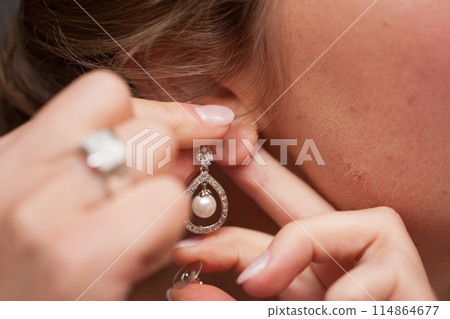 A woman adjusts a pearl earring with a diamond accent, highlighting intricate detail A woman adjusts a pearl earring with a diamond accent, highlighting intricate detail 114864677