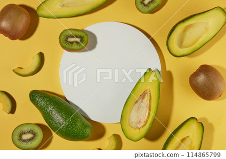 Several slices and halves of avocado and kiwi arranged over yellow background with a white podium. Minimal podium display for cosmetic product presentation Several slices and halves of avocado and kiwi arranged over yellow background with a white podium. Minimal podium display for cosmetic product presentation 114865799