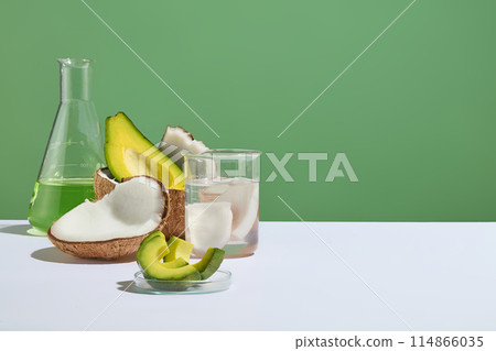 Layout for laboratory concept with some glassware and fresh fruits displayed. Halves of avocado and coconut featured on green background. Product can be showed in the blank space Layout for laboratory concept with some glassware and fresh fruits displayed. Halves of avocado and coconut featured on green background. Product can be showed in the blank space 114866035