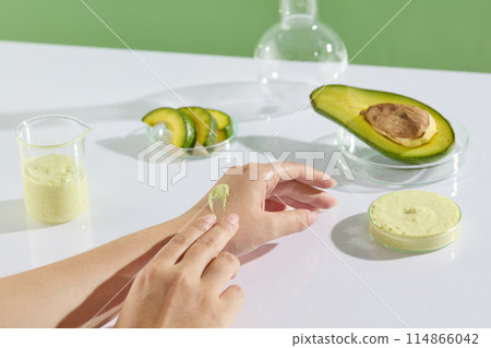 Female hand model is applying avocado cream texture for skincare. Avocado and cream texture contained inside few laboratory glassware. Natural cosmetic concept Female hand model is applying avocado cream texture for skincare. Avocado and cream texture contained inside few laboratory glassware. Natural cosmetic concept 114866042