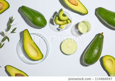 White background with view from above features avocado cut in halves and slices. A beaker and a petri dish containing avocado cream. Copy space White background with view from above features avocado cut in halves and slices. A beaker and a petri dish containing avocado cream. Copy space 114866047