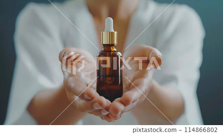 Close up woman hands holding massage or cosmetics oil bottle for applying drops to skin or hair. 114866802