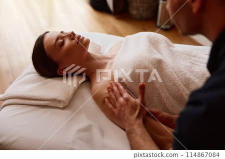 Male masseur massaging arms of relaxing woman client lying on couch 114867084
