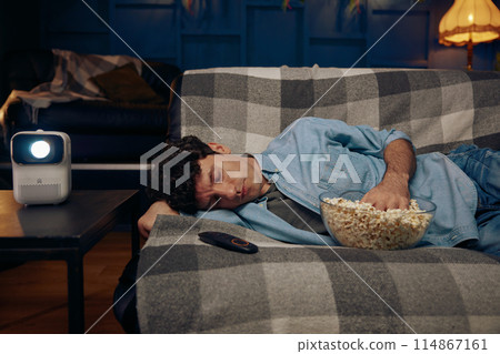 Young man with popcorn sleeping on sofa 114867161