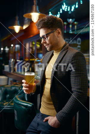 Relaxed businessman with glass of foamy beer in bar 114867180