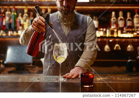 Bartender preparing cool cocktail standing in spray of flying liquid 114867267