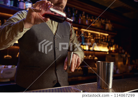 Bartender in uniform pouring drink into shaker behind bar Bartender in uniform pouring drink into shaker behind bar 114867299